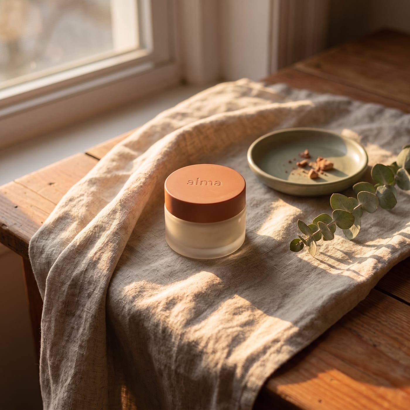 The same jar on sunlit linen beside a ceramic dish and eucalyptus
