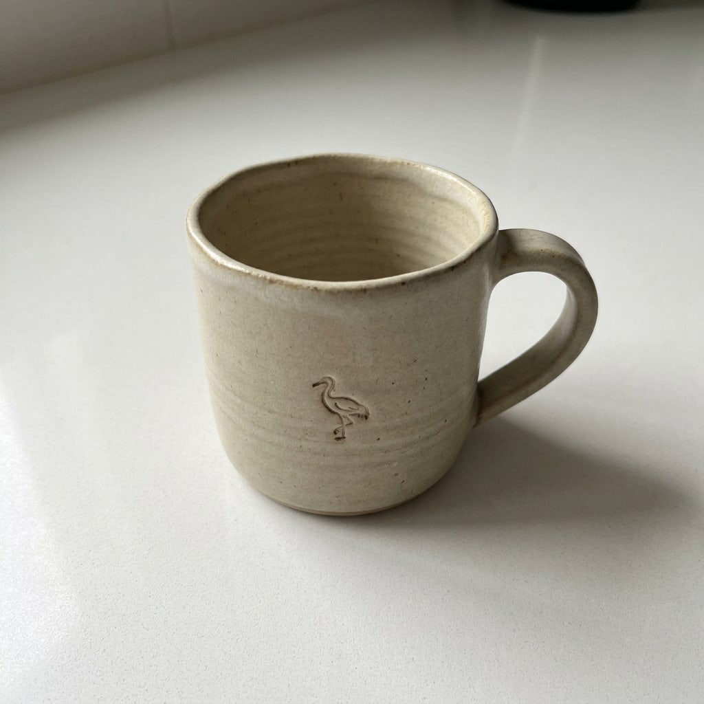 A hand-thrown stoneware mug on a kitchen counter, a small crane stamped into the clay